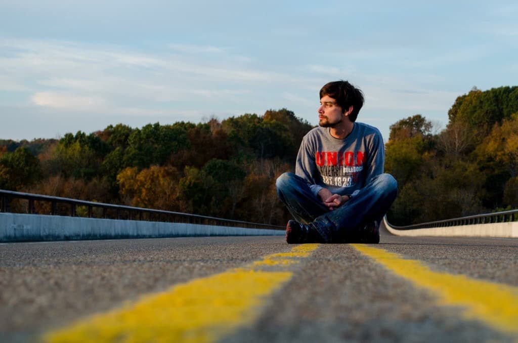 Stephen Rudge sitting on an open road lined with autumn trees
